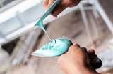 Hands holding a putty knife loaded with creamy, turquoise putty