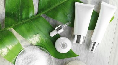 White cosmetic tubes, a dropper bottle, powder, and green leaves, representing biopolymer-based products.