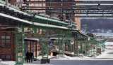 Industrial facility with green metal pipes, brick buildings, and snow covering the ground in a winter landscape.
