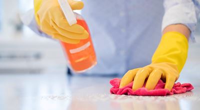 Home and cleaning products. A person wearing yellow rubber gloves is cleaning a surface with a pink cloth and an orange spray bottle