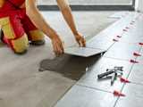 Worker placing tile on tile adhesive pattern on concrete floor.   Secure consistency and improve quality of your building drymix material with our high-quality additives Bermocoll®, Dissolvine® and Expancel®. 