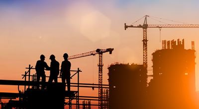 Construction site in morning light. Three workers in the foreground with construction cranes in the background.