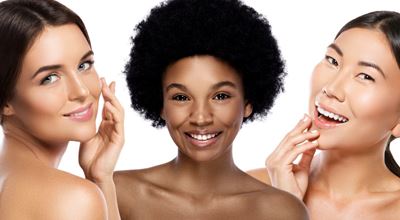 Three women with healthy, glowing skin smiling and gently touching their faces, against a white background.