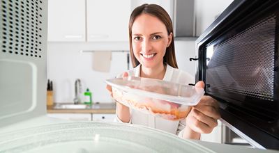 A woman placing a plastic container with food into the microwave