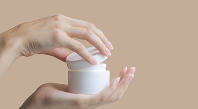 Hands holding and opening a white jar of cream