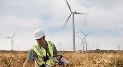 A man wearing a helmet standing in a field with grass, with windmills in the background