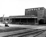 Black and white photo of an Armour factory building with train tracks and a car outside.