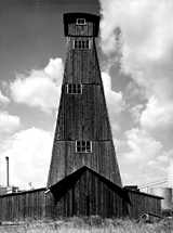Black and white picture of the tall wooden salt mine tower of KNZ, the Royal Dutch salt company, under a partly cloudy sky.