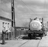 A worker holding a flag guides an EKA Bohus chemical tanker train on tracks in an industrial area.