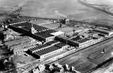 Aerial view of a large factory complex surrounded by farmland and a nearby canal.