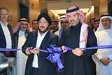 Two men cutting a blue ribbon at an opening ceremony, surrounded by a group of people in formal attire.